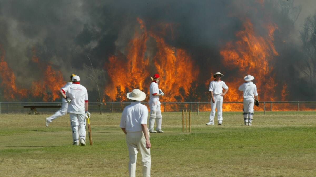 A cricket match carries on in Cessnock, on the central coast, despite a huge bushfire in the background. Photo: DARREN PATEMAN