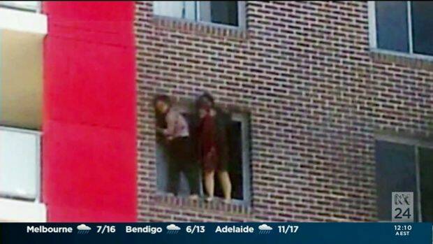 Yinou "Ginger" Jiang and Pingkang "Connie" Zhang cling to the side of their apartment building before being forced to jump. Photo: ABC News 24