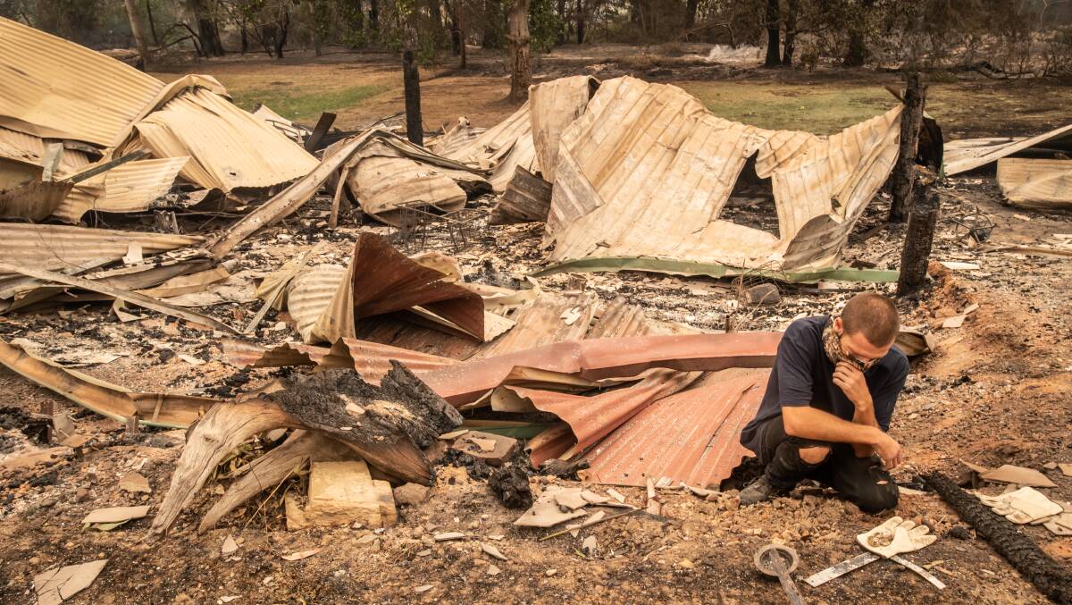 Mogo business owner Karl Niehus sifts through the wreckage of his businesses. One in four businesses in Mogo burnt down during the fires. Picture: Karleen Minney